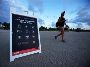 A beachgoer walks past a sign stating new COVID-19 safety measures for the beach on June 10, 2020 in Miami Beach, Florida.