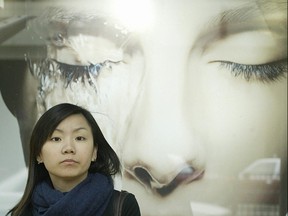 A woman stands by a skin whitening advertisement outside a shop in Hongkong, 19 March 19, 2004.