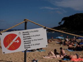 A sign reads "Beach Closed" as people enjoy the sunny weather on Tamariu beach, amid the COVID-19 outbreak in Palafrugell, near Girona, Costa Brava, Spain, June 27, 2020.
