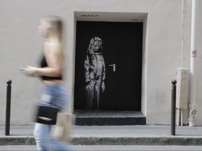In this file photo taken on June 25, 2018, a woman walks past a recent artwork by street artist Banksy in Paris on a side street to the Bataclan concert hall where a terrorist attack killed 90 people on Nov. 13, 2015.
