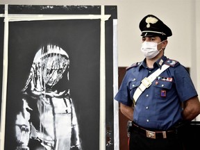 An Italian Carabinieri poses near a piece of art attributed to Banksy, that was stolen at the Bataclan in Paris in 2019, and found in Italy, during a press conference in L'Aquila, June 11, 2020.
