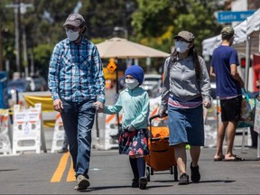 In this file photo taken on May 3, 2020 a familly wearing masks walk at the West LA Farmer's Market in Santa Monica, California.