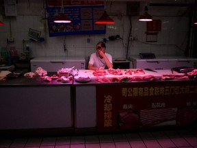 A pork vendor wearing a face mask uses his phone as he waits for customers at a meat stall inside a grocery market, following new cases of COVID-19 infections in Beijing, China, Monday, June 15, 2020.