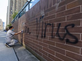A man cleans graffiti on the Chinese consulate's wall in Calgary Wednesday, May 27, 2020.