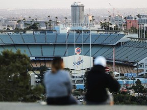 People sit on a hill overlooking Dodger Stadium on what was supposed to be Major League Baseball's opening day on March 26, 2020 in Los Angeles.