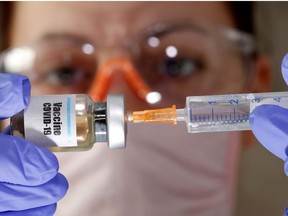 A woman holds a small bottle labeled with a "Vaccine COVID-19" sticker and a medical syringe in this illustration taken April 10, 2020.