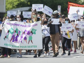 People hold up signs during a demonstration outside Prime Minister Justin Trudeau's constituency office in Montreal, Saturday, June 6, 2020, where they called on the government to give residency status to migrant workers as the COVID-19 pandemic continues in Canada and around the world.