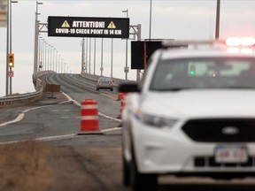 An RCMP vehicle is parked in front of the Confederation Bridge as a vehicle passes under a warning sign of COVID-19 checkpoint on Prince Edward Island at Cape Jourimain, New Brunswick, April 2, 2020.
