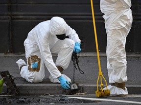 Police forensics officers dressed in Tyvek protective suits and wearing masks, conduct a search of a drain near Forbury Gardens park in Reading, on June 22, 2020.