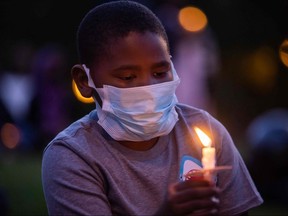 A boy holds a candle during a vigil around a makeshift memorial at the tree where Robert Fuller was found dead outside Palmdale City Hall on June 13, 2020.