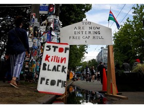 People walk by signs at a barrier set up at the edge of the self-proclaimed CHAZ/CHOP zone around the Seattle Police Department's East Precinct as people call for the defunding of police and protest against racial inequality in the aftermath of the death in Minneapolis police custody of George Floyd, in Seattle, Washington, U.S. June 14, 2020.