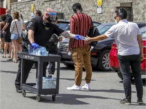 Security guard Jean-François Monette gives out bottles of water to people lined up for testing at the Hôtel-Dieu site in Montreal on Sunday, July 12, 2020.