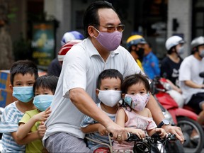 A man and his children, all wearing protective masks, ride a bicycle on a street during the coronavirus disease (COVID-19) outbreak, in Hanoi, Vietnam July 27, 2020.