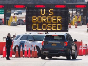 In this file photo US Customs officers speaks with people in a car beside a sign saying that the US border is closed at the US/Canada border in Lansdowne, Ontario, on March 22, 2020.