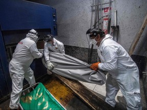 In this file photo taken on June 11, 2020, employees of the Iztapalapa pantheon manoeuvre to put a body bag with the remains of a victim of COVID-19 in an oven at the crematorium, in Mexico City, amid the novel coronavirus pandemic.