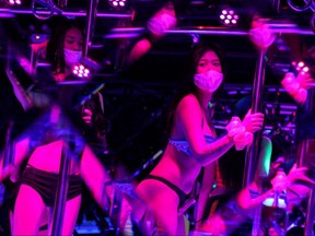 Women wearing face masks are reflected in a mirror as they dance inside the XXX Lounge at Thailand's legendary Patpong nightlife and sex trade district after the Thai government eased isolation measures and introduced social distancing to prevent the spread of COVID-19, as bars and nightclubs are reopened nationwide in Bangkok, Thailand, Wednesday, July 1, 2020.