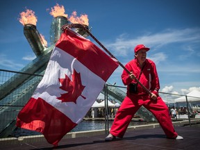 Ricky Johnson waves a Canadian flag on a hockey stick as the Olympic cauldron burns while attending Canada Day celebrations in Vancouver, on July 1, 2019.