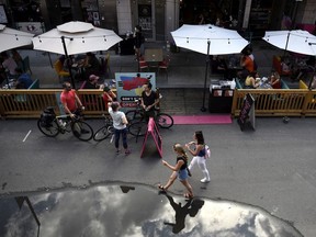 People sit in outdoor booths, built on top of street parking spots outside a restaurant as people walk on a road closed to car traffic in the Byward Market in Ottawa, on Sunday, July 12, 2020, in the midst of the COVID-19 pandemic.