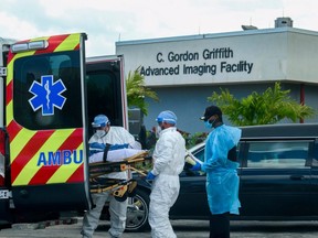 Emergency Medical Technicians arrive with a patient while a funeral car begins to depart at North Shore Medical Center where COVID-19 patients are treated, in Miami, July 14, 2020.