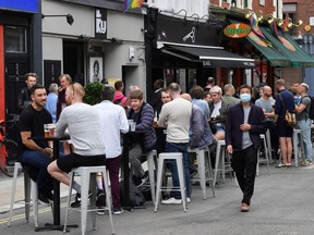 Customers sit outside re-opened bars in Soho in London as the area embraces pedestrianization in line with an easing of restrictions during the COVID-19 pandemic, Saturday, July 4, 2020.