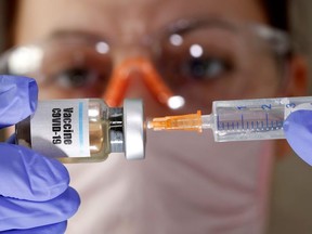 A woman holds a small bottle labeled with a "Vaccine COVID-19" sticker and a medical syringe in this illustration taken April 10, 2020.