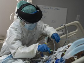 A member of the medical staff wearing full PPE brushes a patient's teeth in the COVID-19 intensive care unit at the United Memorial Medical Center in Houston, Tuesday, June 30, 2020.