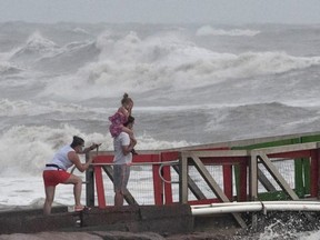 A girl covers her face from strong winds as her family members watch high swells from Hurricane Hanna from a jetty in Galveston, Texas, Saturday, July 25, 2020.