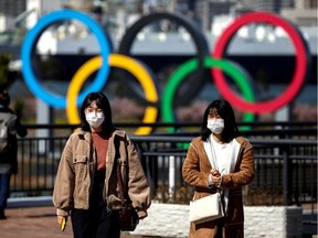 People wearing protective face masks, following an outbreak of the coronavirus, are seen in front of the Giant Olympic rings at the waterfront area at Odaiba Marine Park in Tokyo, Japan, February 27, 2020.
