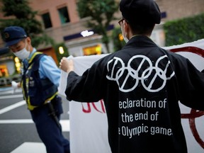 A demonstrator wearing a face mask holds a sign to protest against the Tokyo 2020 Olympic Games a year before the start of the summer games that have been postponed to 2021 due to COVID-19, near the National Stadium in Tokyo, Friday, July 24, 2020.