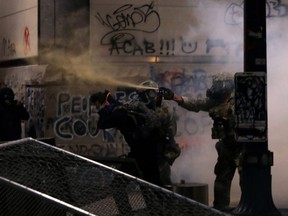 Federal law enforcement officers, deployed under the Trump administration's executive order to protect federal monuments and buildings, use pepper spray and tear gas on demonstrators during a protest against racial inequality in Portland, Ore., Saturday, July 18, 2020.