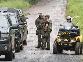 Police officers pause as they search a back road on Saturday, July 11, 2020 in Saint-Apollinaire, Quebec. Quebec provincial police say two girls who were the subject of an Amber Alert have been found dead.