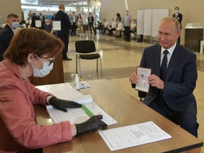 Russian President Vladimir Putin shows his passport to a member of a local electoral commission as he arrives to cast his ballot in a nationwide vote on constitutional reforms at a polling station in Moscow, Wednesday, July 1, 2020.