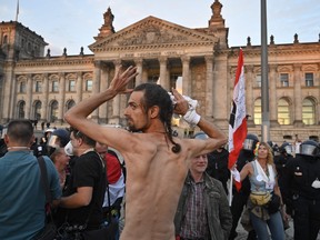 A protester stands half naked and lifts his hands up in front of the Reichstag building guarded by policemen at the end of a demonstration called by far-right and COVID-19 deniers to protest against restrictions related to the new coronavirus pandemic, in Berlin, on Aug. 29, 2020.
