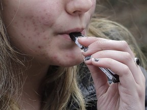 In this April 11, 2018, file photo, a high school student uses a vaping device near a school campus in Cambridge, Mass.