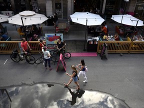 People sit in outdoor booths, built on top of street parking spots outside a restaurant as people walk on a road closed to car traffic in the Byward Market in Ottawa, on Sunday, July 12, 2020. A