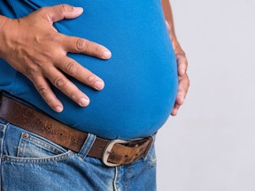 Overweight or fat adult man in very tight jeans on a gray background. Healthcare, medicine concept.