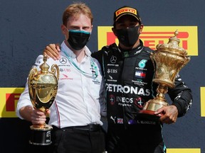 Mercedes' Lewis Hamilton and a team member celebrate winning the race on the podium with the trophies.