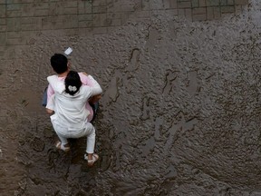 A man crosses a mud-covered trail carrying his wife on his back at a flooded Han River park in Seoul, South Korea, August 4, 2020.