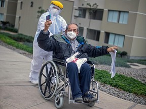 In this file photo taken on August 28, 2020 Cesar Sayan, who recovered from COVID-19, gestures as he is pushed on a wheelchair by a health worker after being discharged from the Villa Panamericana.