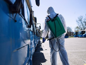 Man in a white protective suit with reservoir spraying disinfectant on parked buses.