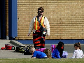 A school employee watches over some students at Waverley Elementary School in Edmonton on Friday Sept., 18, 2020, where a COVID-19 outbreak has been declared. Two students from the school tested positive for the virus. Twelve students and seven staff members have been ordered to self-isolate at home for 14 days. This is the first documented case of in-school COVID-19 transmission in Alberta since the beginning of the school year.