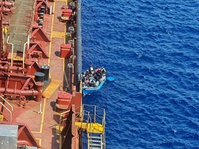 Migrants sit in a boat alongside the Maersk Etienne tanker off the coast of Malta, in this handout image provided August 19, 2020.