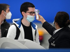 In this file photo taken on July 10, 2020 passengers wearing masks or covering due to the COVID-19 pandemic, have their temperature taken as they queue at Heathrow airport.