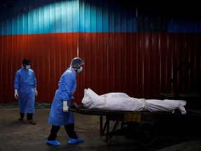 A health worker wearing personal protective equipment carries the body of a man, who died due to COVID-19, at a crematorium in New Delhi, India, Monday, Sept. 7, 2020.