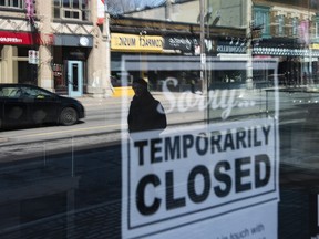 Storefronts in Ottawa's Glebe neighbourhood are reflected in a sign indicating the temporary closure of a business to prevent the spread of COVID-19, on Tuesday, March 24, 2020.