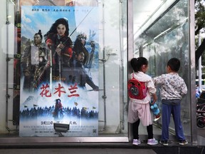 Children play next to a poster of the Disney movie "Mulan" outside a cinema in Beijing on September 11, 2020.