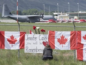 The Canadian Forces Snowbirds jets are seen in the background as a woman attaches a sign to a fence in Kamloops, B.C., Monday, May 18, 2020.
