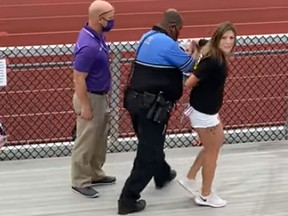 A woman is led away after being Tasered and arrested for not wearing a mask at a football game in Logan, Ohio.