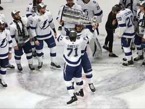 Tampa Bay Lightning's Anthony Cirelli hands off the Stanley Cup to Mikhail Sergachev.