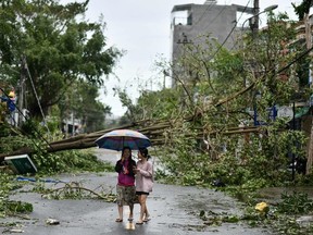 Women walk past uprooted trees in central Vietnam's Quang Ngai province on October 28, 2020, in the aftermath of Typhoon Molave.